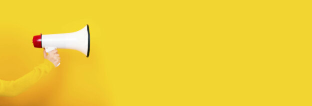megaphone in hand on a yellow background, panoramic image, attention concept announcement